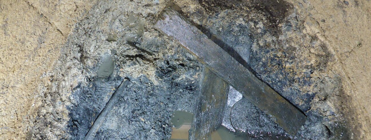 Soubor prken na povrchu fekálního sedimentu – pozůstatky dřevěné konstrukce latrín.